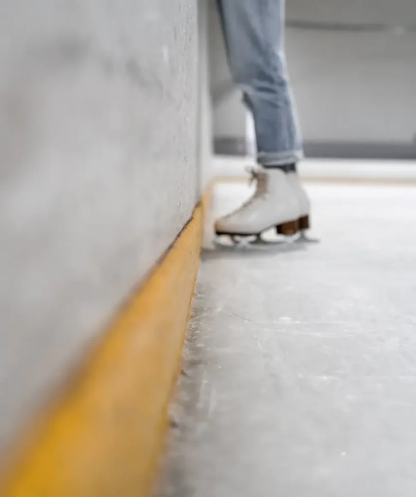 Vi ser benen av en människa i jeans och konståknings-skridskor i rinken på väg ut från rinken.