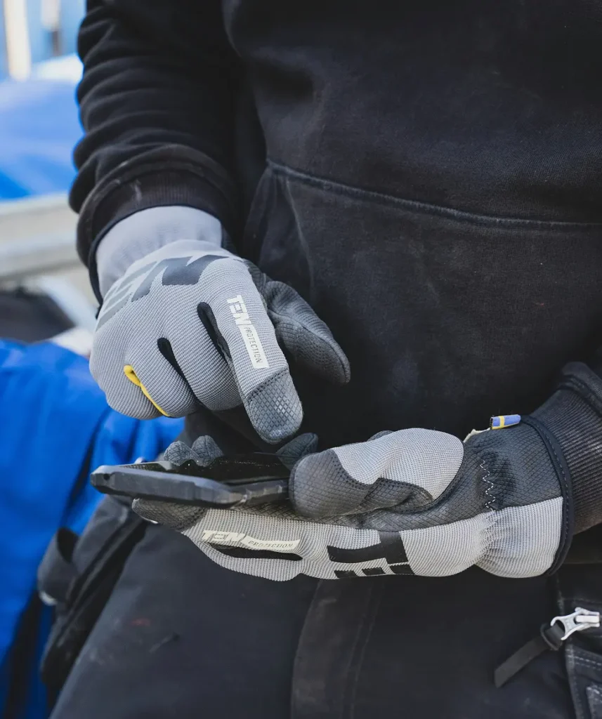 En man i arbetskläder och handskar integrerar med en mobil.